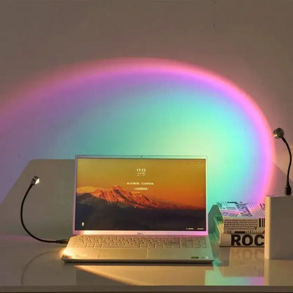 USB Sunset Projection Lamp casting colorful light over a laptop and desk in a cozy setting.